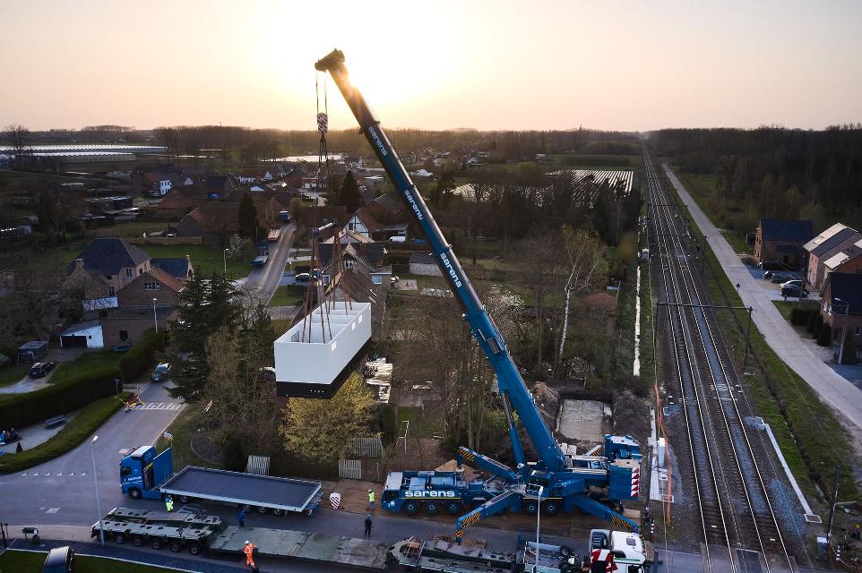 Alfen Sarens hydraulische kraan plaatsing electrische cabine naast spoorlijn dronefoto bij zonsondergang