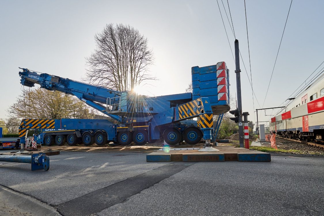 Sarens hydraulische kraan naast spoor met trein