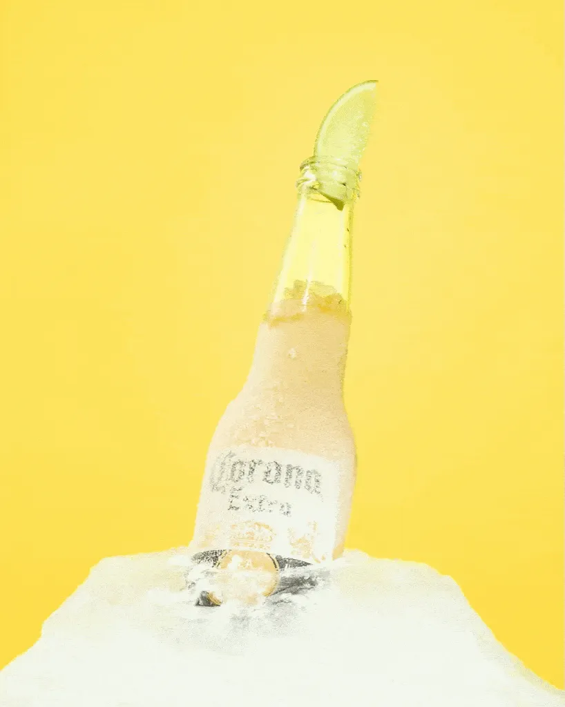 Een fles Corona Extra met een partje limoen, ingevroren in een blok ijs, op geel, Studio Ballena